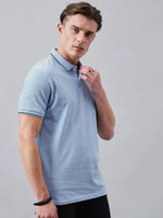 Man wears 98degreenorth Men's Sky Blue Solid Polo T-Shirt—Cotton Pique, standing against a plain gray background.