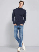 Man in 98degreenorth Men’s Teal Blue Merino Wool Turtle Neck Sweater, blue jeans, and white sneakers.