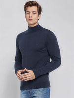 Man in 98degreenorth Men’s Teal Blue Merino Wool Turtle Neck Sweater and jeans, against a light gray background.