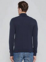 Man in a 98degreenorth teal blue merino wool turtle neck sweater and blue jeans, facing away from the camera.