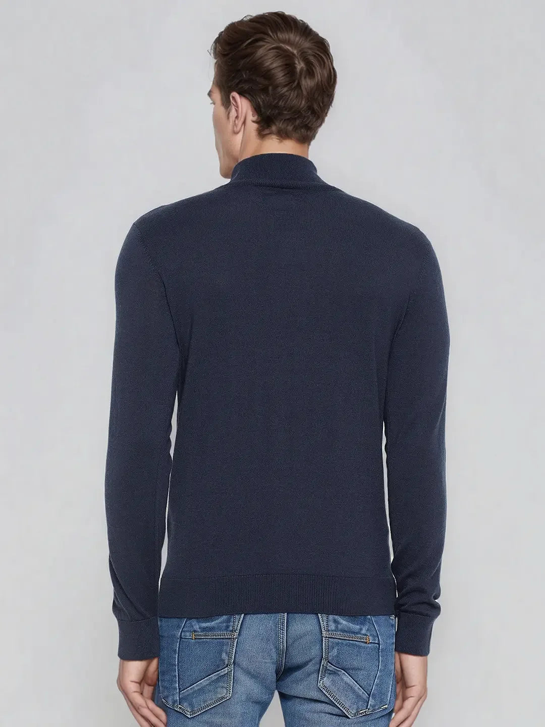 Man in a 98degreenorth teal blue merino wool turtle neck sweater and blue jeans, facing away from the camera.