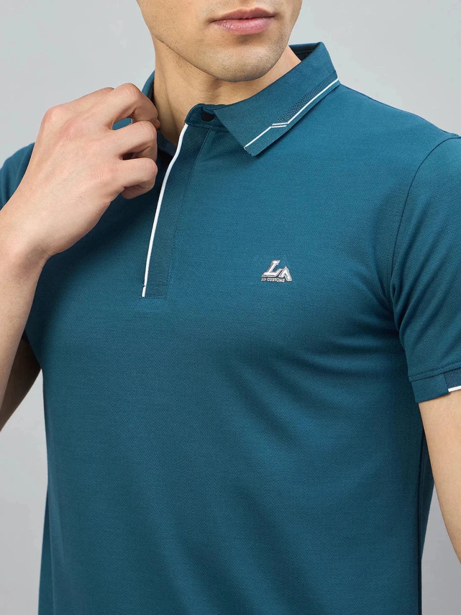 Man wearing 98degreenorth Men's Teal Polo T-Shirt with White Tipping and LA logo, touching the collar.