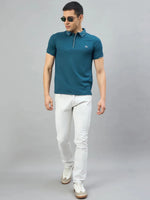 Man in 98degreenorth Men's Teal Polo T-Shirt with LA Logo, white jeans, and sneakers on a plain grey background.
