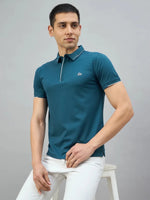 Man in a 98degreenorth teal polo with white tipping and LA logo sits on a stool, looking to the side.