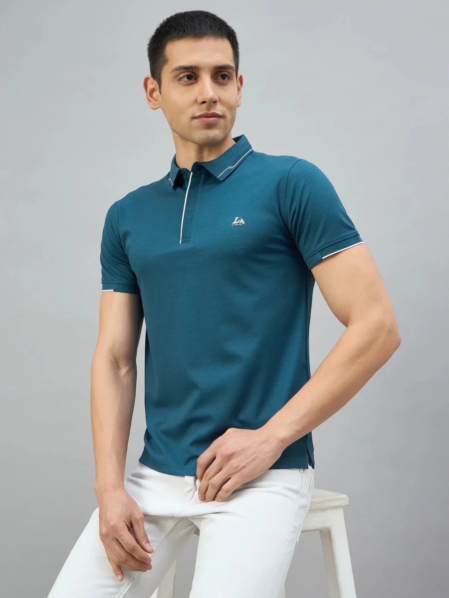 Man in a 98degreenorth teal polo with white tipping and LA logo sits on a stool, looking to the side.