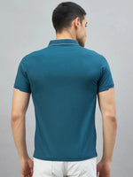 Man in a 98degreenorth men's teal polo with LA logo and white shorts, back to camera on plain background.