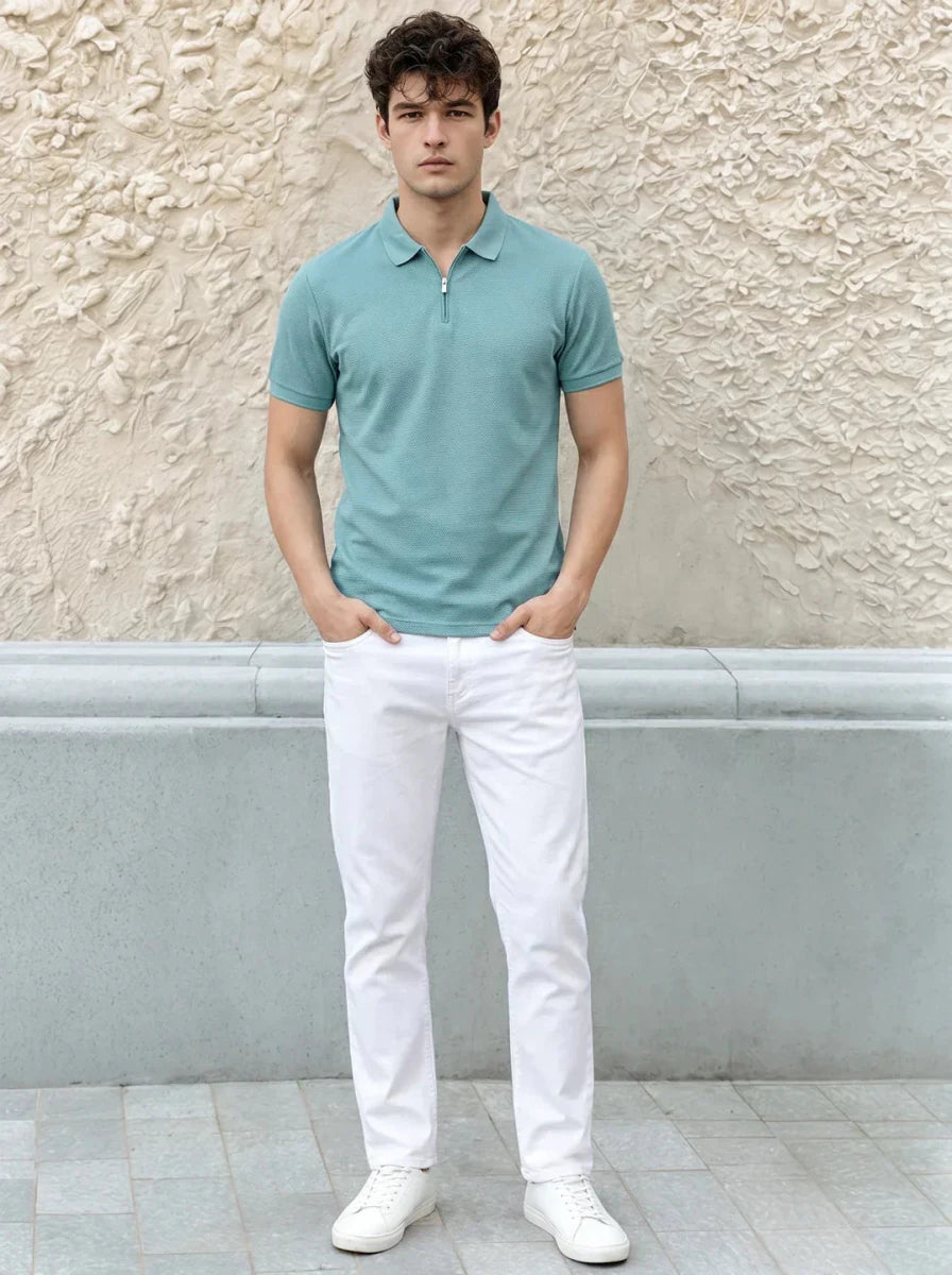 A man in a turquoise 98degreenorth quarter zip polo stands against a textured beige wall.