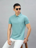 Man in sunglasses wears the 98degreenorth Men's Turquoise Quarter Zip Polo T-Shirt, sitting on a wooden stool.