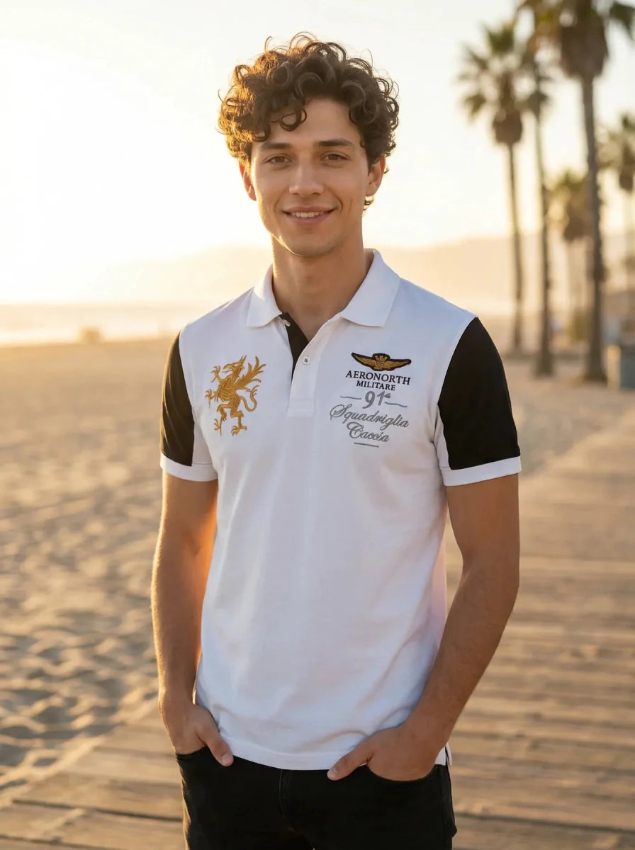Smiling man in a Men's White Black Sleeve Aeronorth 91ª Polo by 98degreenorth stands on a sunny palm-lined boardwalk.