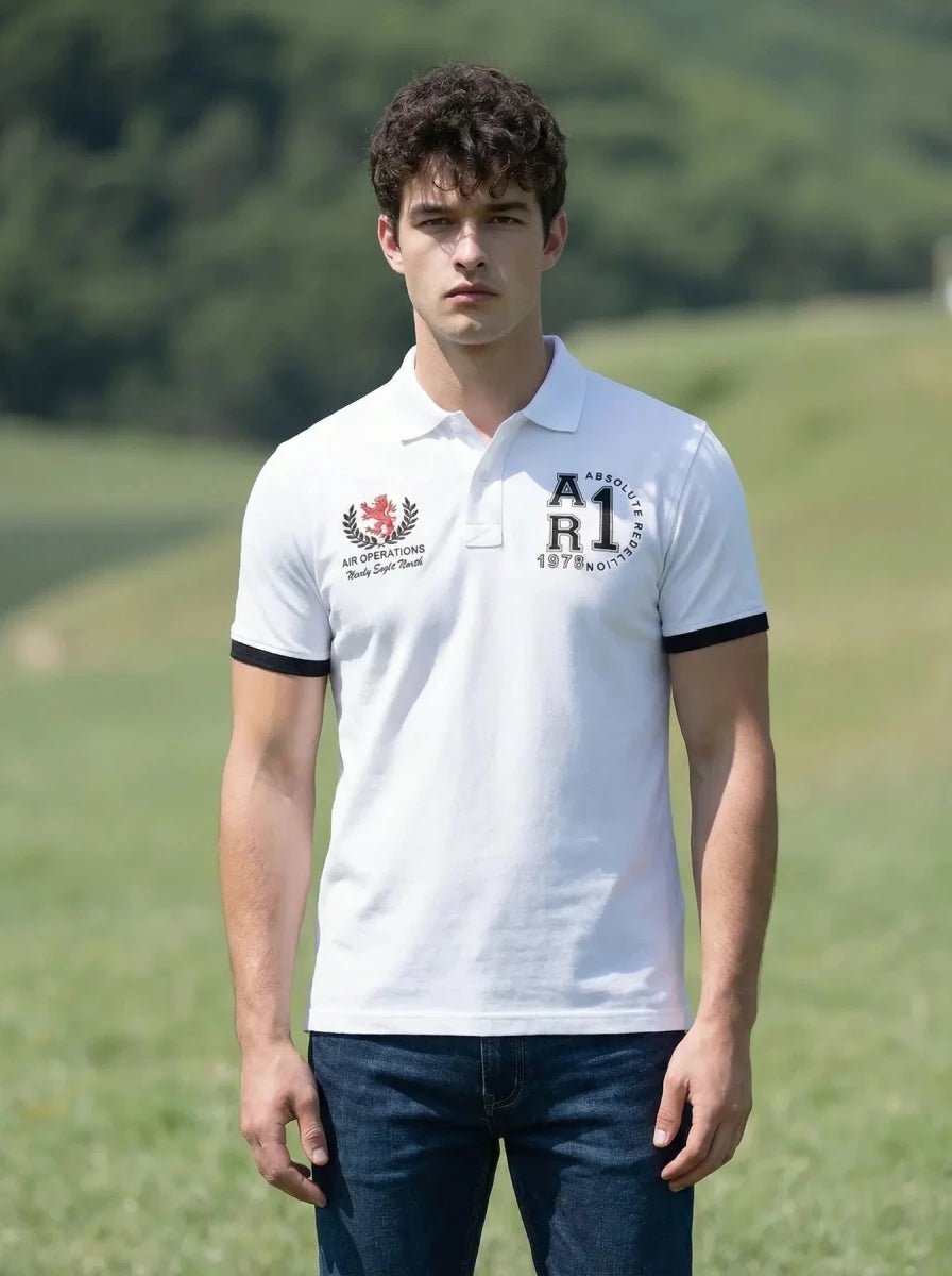 Young man wears a 98degreenorth Men's White Embroidered Polo T-Shirt, standing on grass with trees behind him.