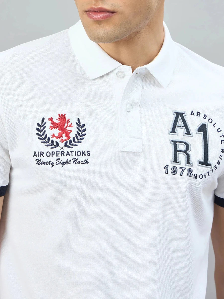 Man wears 98degreenorth Men's White Embroidered Polo T-Shirt with text and a red lion chest emblem.
