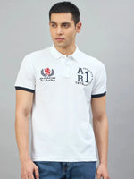 Man wearing the 98degreenorth Men's White Embroidered Polo T-Shirt and blue jeans, standing against a gray background.