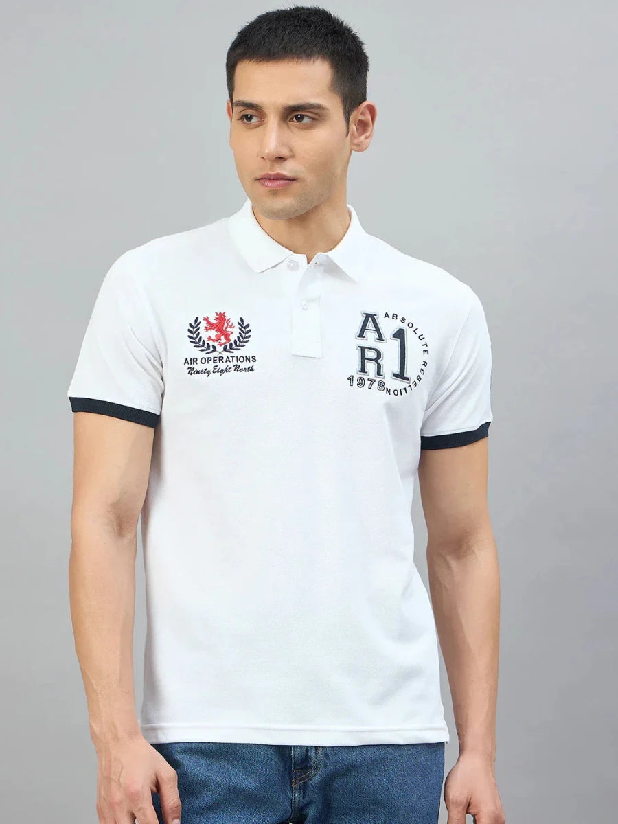 Man wearing the 98degreenorth Men's White Embroidered Polo T-Shirt and blue jeans, standing against a gray background.