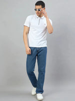 Man wears 98degreenorth Men's White Polo T-Shirt with Navy Tipping, blue jeans, and sneakers against a gray background.