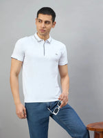 Man wears 98degreenorth Men's White Polo T-Shirt with Navy Tipping, holding sunglasses beside a stool on gray background.