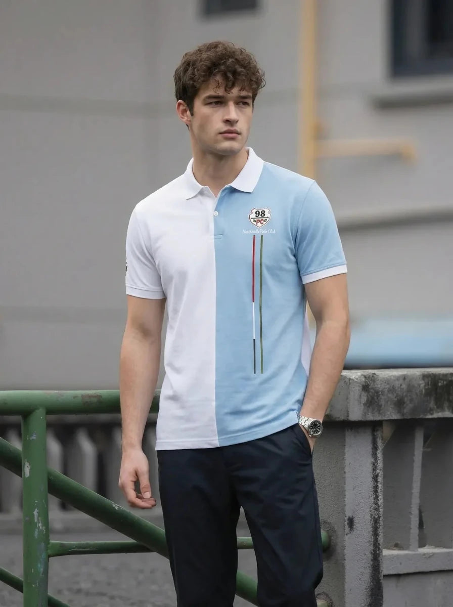 A man in a 98degreenorth Men's White Sky Blue Colour Block Polo T-Shirt stands outdoors by a green railing.
