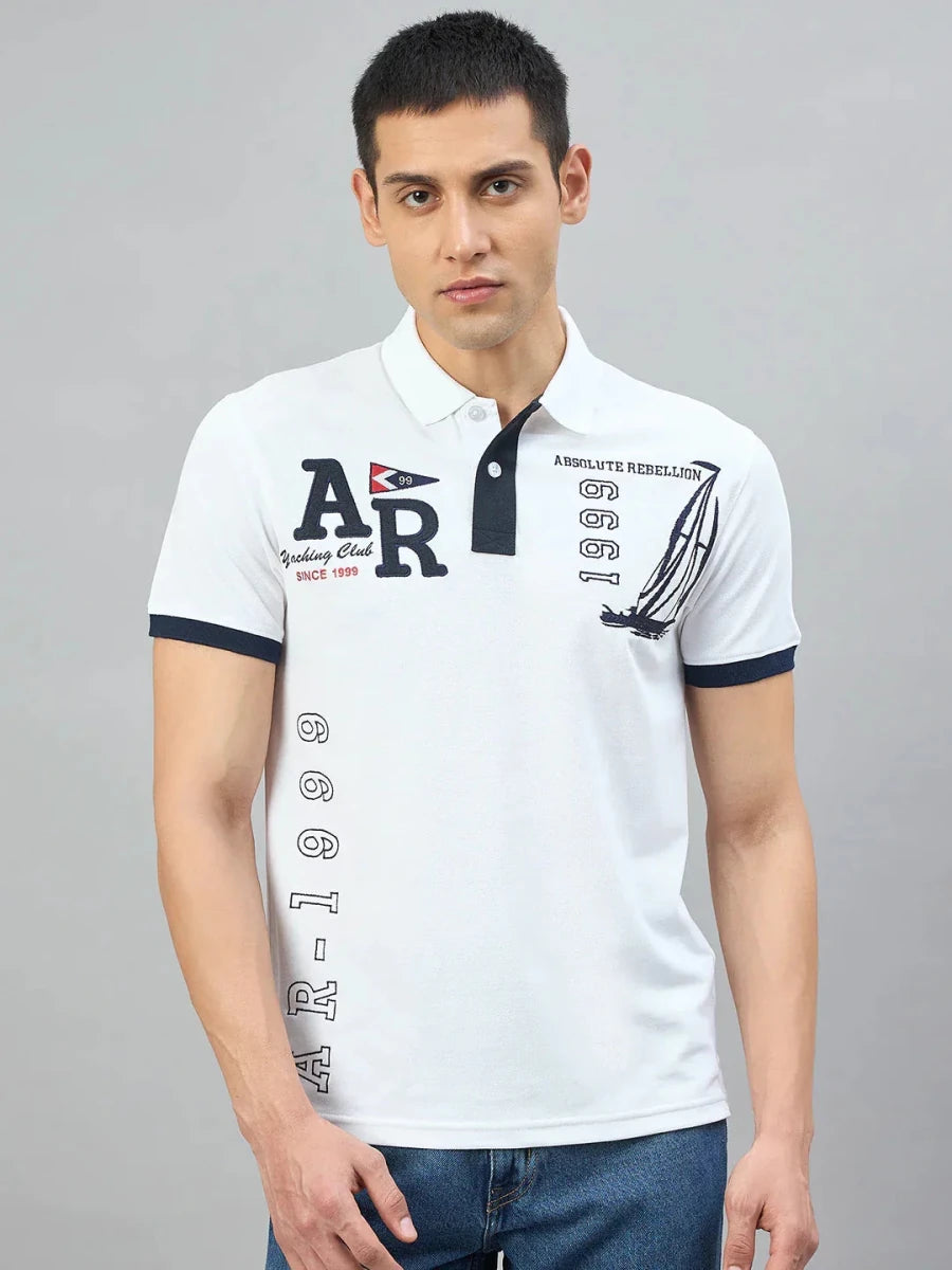 Man wearing 98degreenorth Men's White Yachting Club Polo T-Shirt and blue jeans, standing against a gray background.
