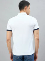 Man wears 98degreenorth Men's White Yachting Club Polo T-Shirt, paired with blue jeans, facing away against plain backdrop.