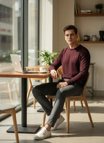 Man in a 98degreenorth Men’s Wine Merino Wool Sweater sits at a cafe table with laptop, coffee, and glasses.