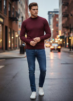 A man in a 98degreenorth Men’s Wine Merino Wool Turtle Neck Sweater walks down a city street at dusk.