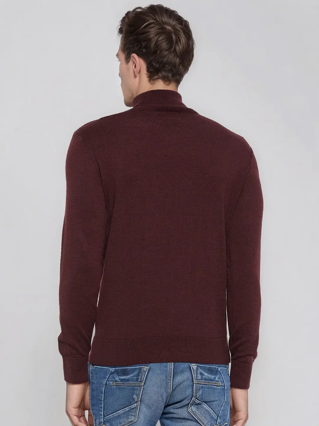 Man in 98degreenorth Men’s Wine Merino Wool Turtle Neck Sweater, standing in blue jeans against a plain light background.