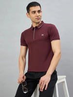 Man in a 98degreenorth Men's Wine Polo T-Shirt with White Tipping and black jeans, holding sunglasses, seated on a stool.