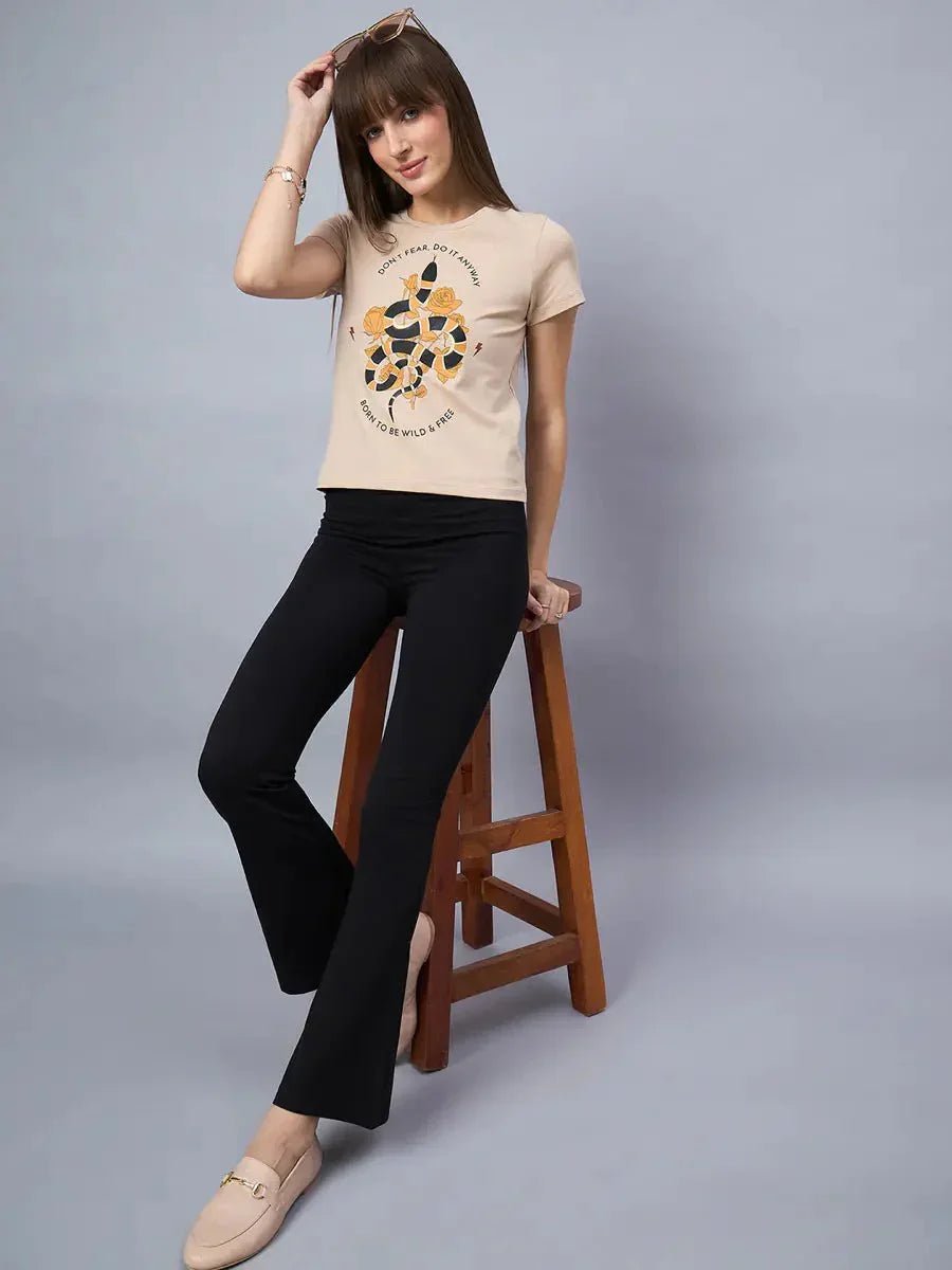 Woman in 98degreenorth Minimal Typography Print cotton tee, black pants, and loafers sits on a stool against gray backdrop.