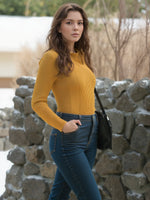 Woman wears 98degreenorth Mustard Yellow Ribbed Collared Sweater, posing confidently by a stone wall outdoors.