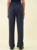 Woman models 98degreenorth Navy Wide Leg Pintuck Trackpants from Luxe Lounge, shown from the back against a plain backdrop.