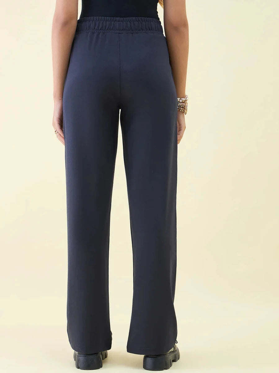 Woman models 98degreenorth Navy Wide Leg Pintuck Trackpants from Luxe Lounge, shown from the back against a plain backdrop.