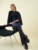 Woman in Navy Wide Leg Pintuck Trackpants by 98degreenorth, sitting sideways on a chair against a light backdrop.