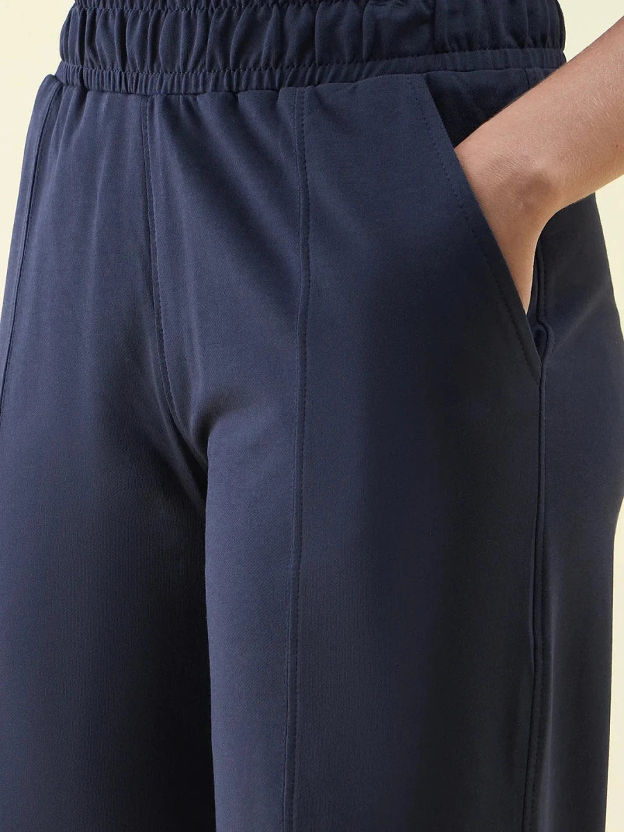 Close-up of a person wearing 98degreenorth Navy Wide Leg Pintuck Trackpants with right hand in pocket.