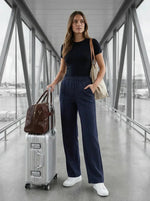 Woman in navy Wide Leg Pintuck Trackpants by 98degreenorth stands at airport with suitcase, tote, and duffel.