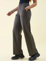 Woman in 98degreenorth Olive Wide Leg Pintuck Trackpants, black top and shoes, standing with one hand in her pocket.