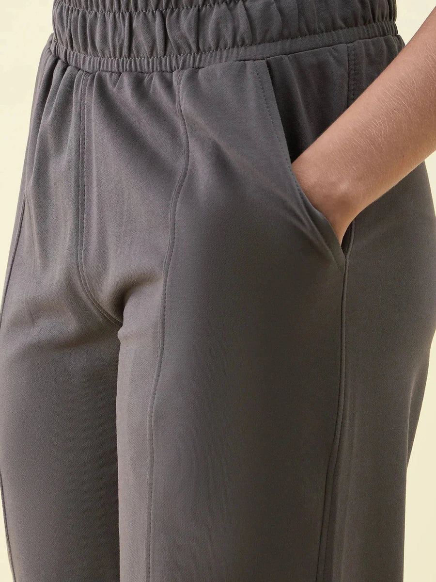 A person in 98degreenorth Olive Wide Leg Pintuck Trackpants, one hand in pocket, shown waist to mid-thigh.