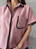 A woman wears the 98degreenorth Pink Whipstitch Trim Cotton Shirt with black trim on collar, pocket, and sleeves.