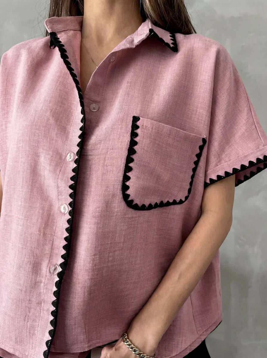 A woman wears the 98degreenorth Pink Whipstitch Trim Cotton Shirt with black trim on collar, pocket, and sleeves.