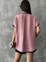 A person with long hair wears the 98degreenorth Pink Whipstitch Trim Cotton Shirt, posing by a gray textured wall.