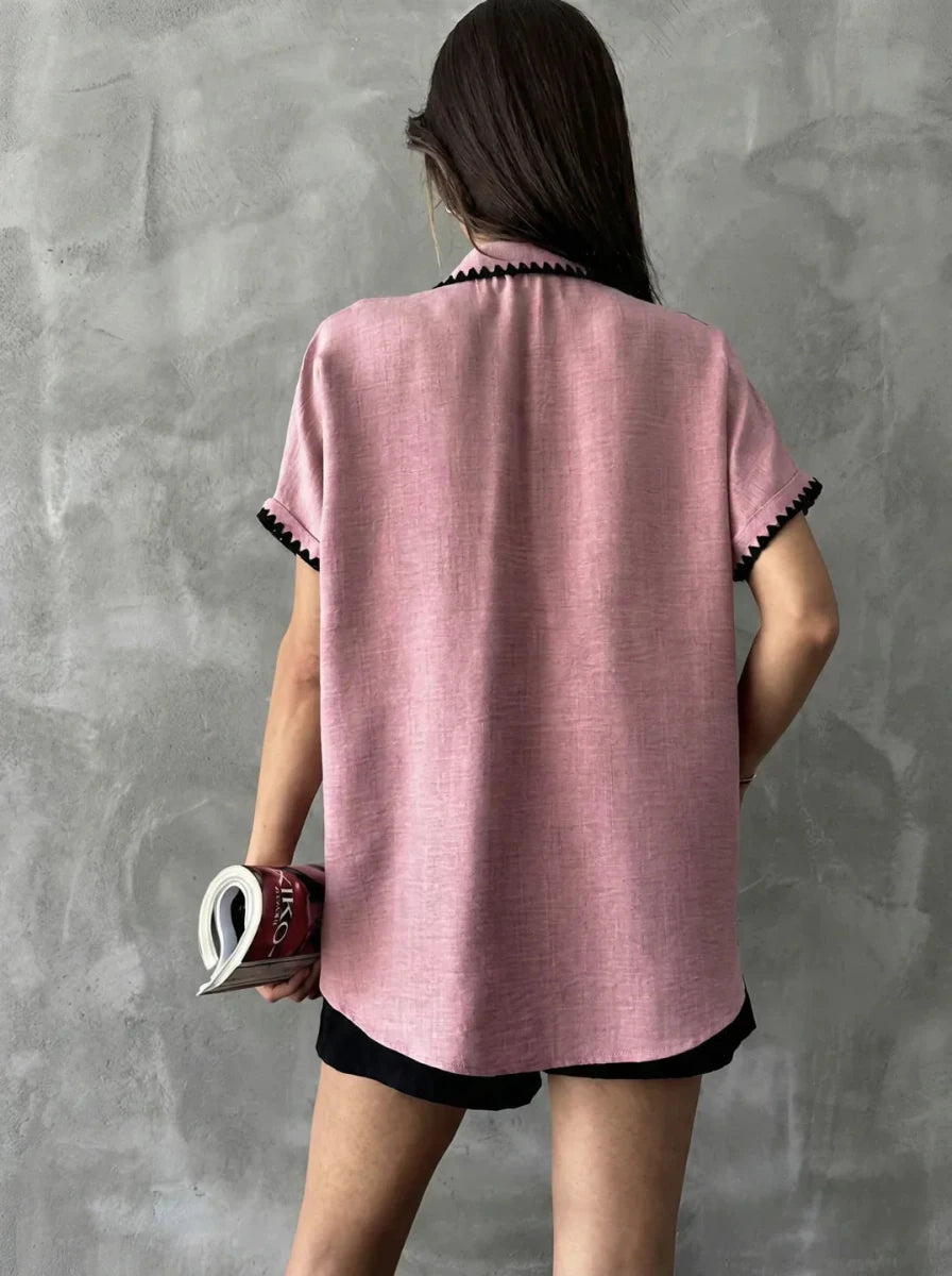A person with long hair wears the 98degreenorth Pink Whipstitch Trim Cotton Shirt, posing by a gray textured wall.