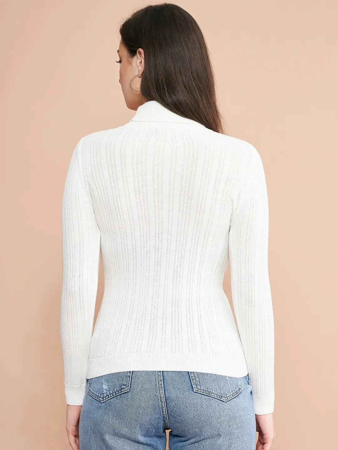 A woman with long brown hair, wearing the 98degreenorth Ribbed White Turtle Neck Pullover and blue jeans, stands with her back to the camera against a beige background.