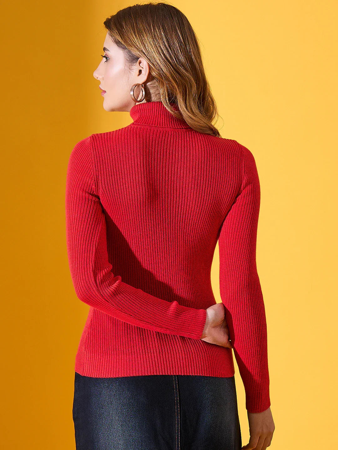 Woman in a 98degreenorth Scarlet Red Ribbed Turtleneck Sweater, standing against a yellow background.