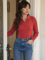 Woman in a 98degreenorth Scarlet Red Ribbed Collared Sweater and high-waisted jeans stands by a door, looking aside.