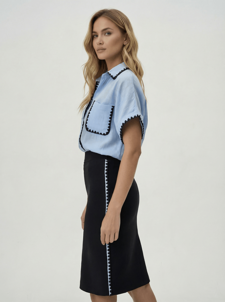 Woman in a 98degreenorth Sky Blue Whipstitch Trim Cotton Shirt from Luxe Summer, paired with a black skirt.