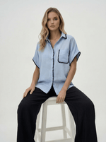 Woman wears 98degreenorth Sky Blue Whipstitch Trim Cotton Shirt and black pants, Luxe Summer collection.