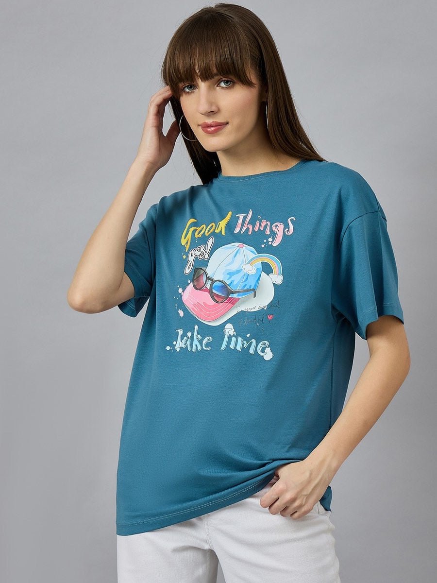 Woman in 98degreenorth Trendy Typography Graphic T-shirt poses in white pants against a plain gray background.