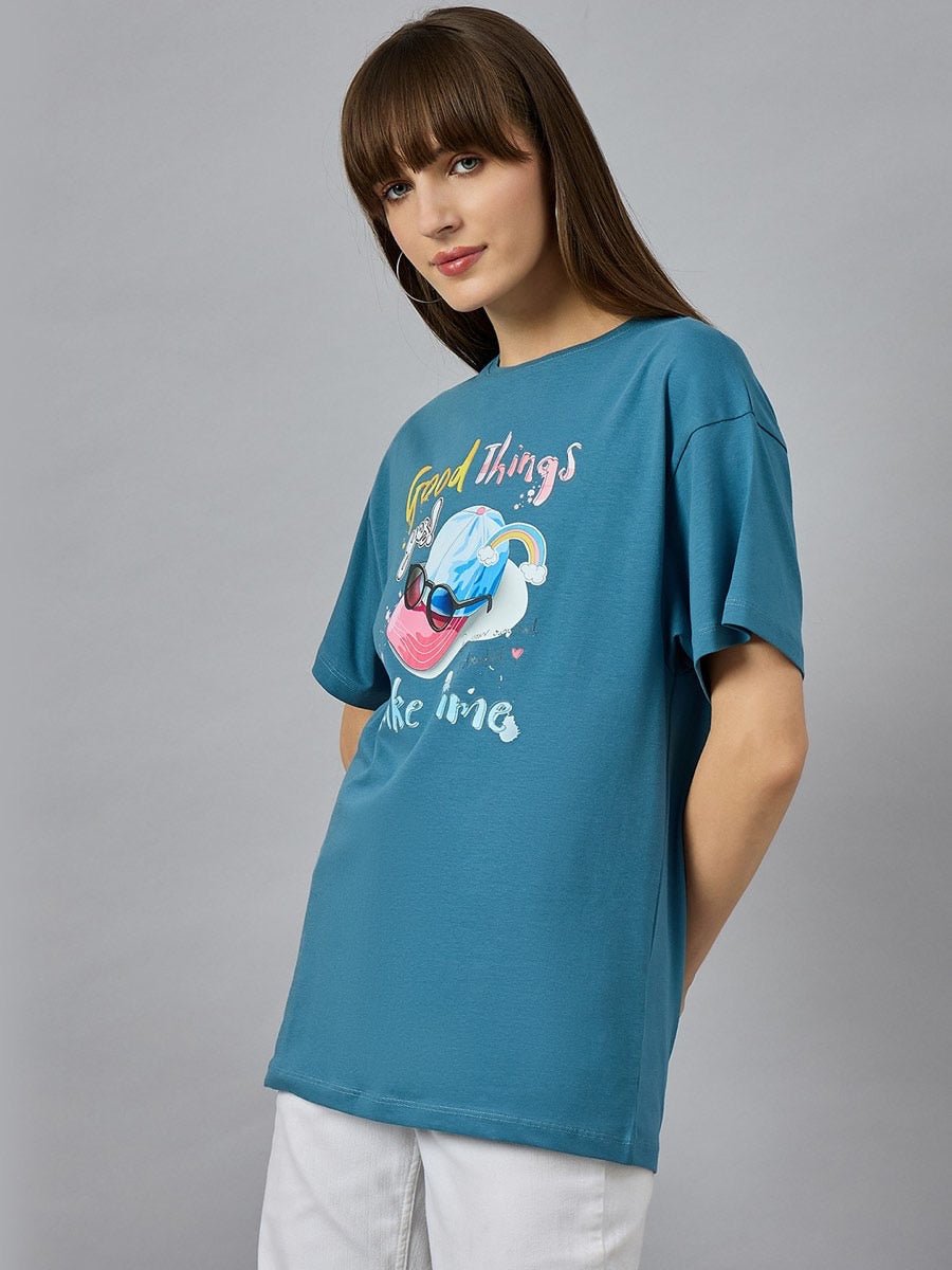 Woman in a 98degreenorth Trendy Typography Graphic T-shirt – cotton, round neck, drop shoulder – with white pants.