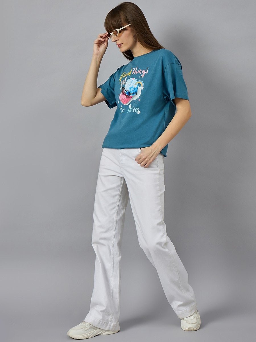 Woman in sunglasses sports a 98degreenorth Typography Graphic T-shirt, white pants & sneakers for an urban look.