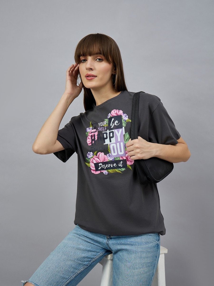 Woman in 98degreenorth Typography Graphic Cotton Tee—drop shoulder sleeves, casual wear—sits on a stool with a black bag.