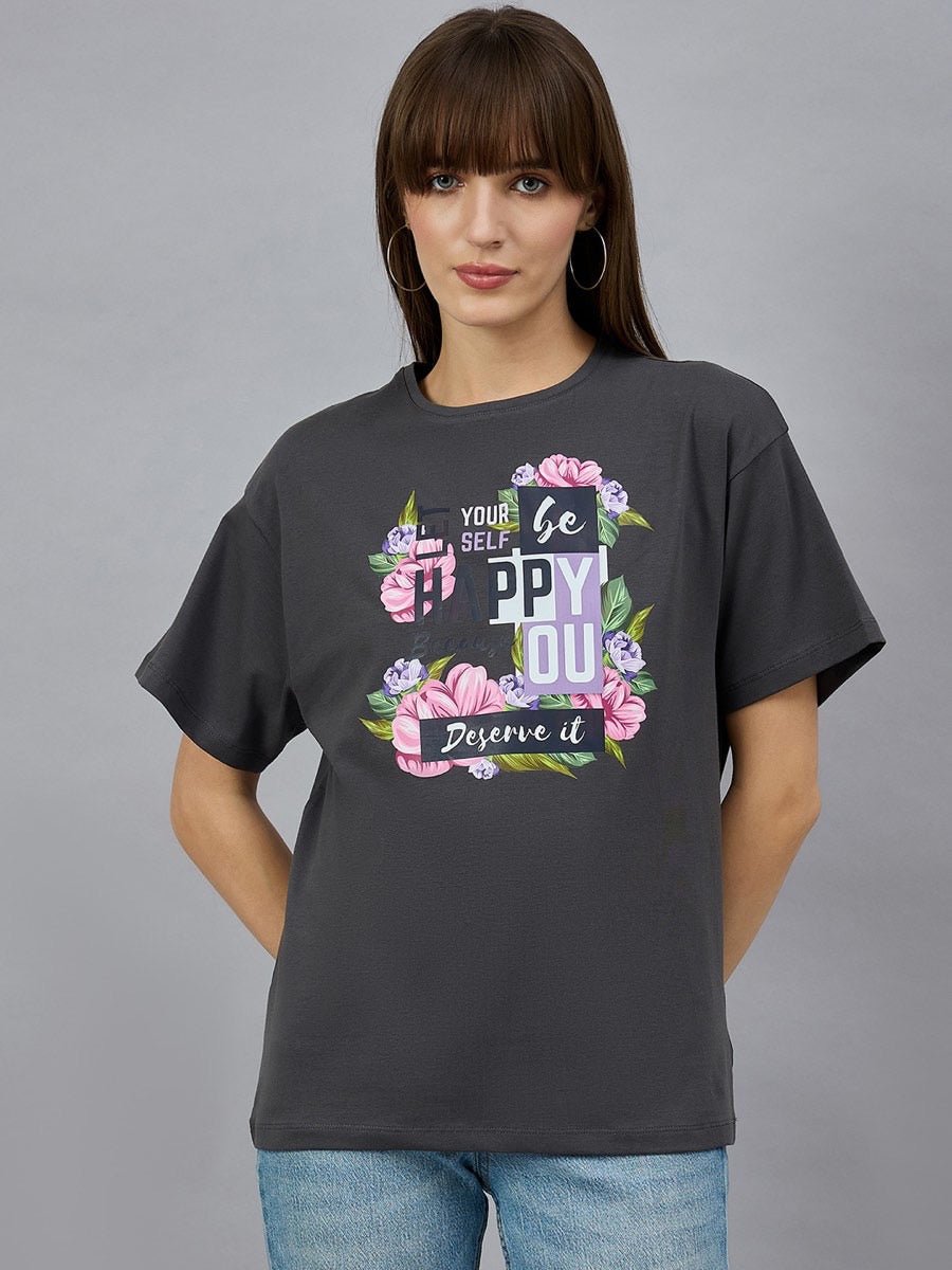 Woman wearing the 98degreenorth Typography Graphic Cotton Tee with drop shoulder sleeves, standing against a gray background.
