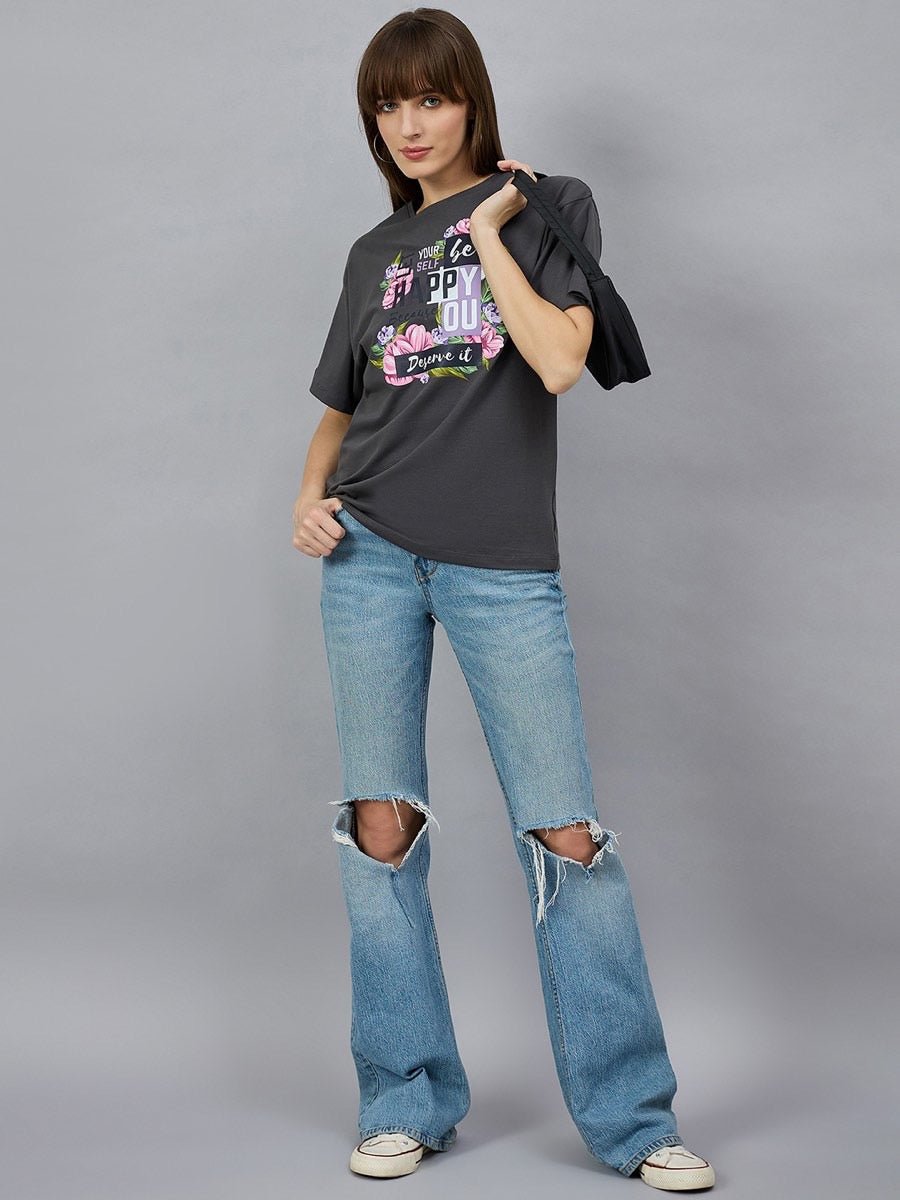 Woman models 98degreenorth Typography Graphic Cotton Tee with drop shoulders, styled casually against a gray backdrop.